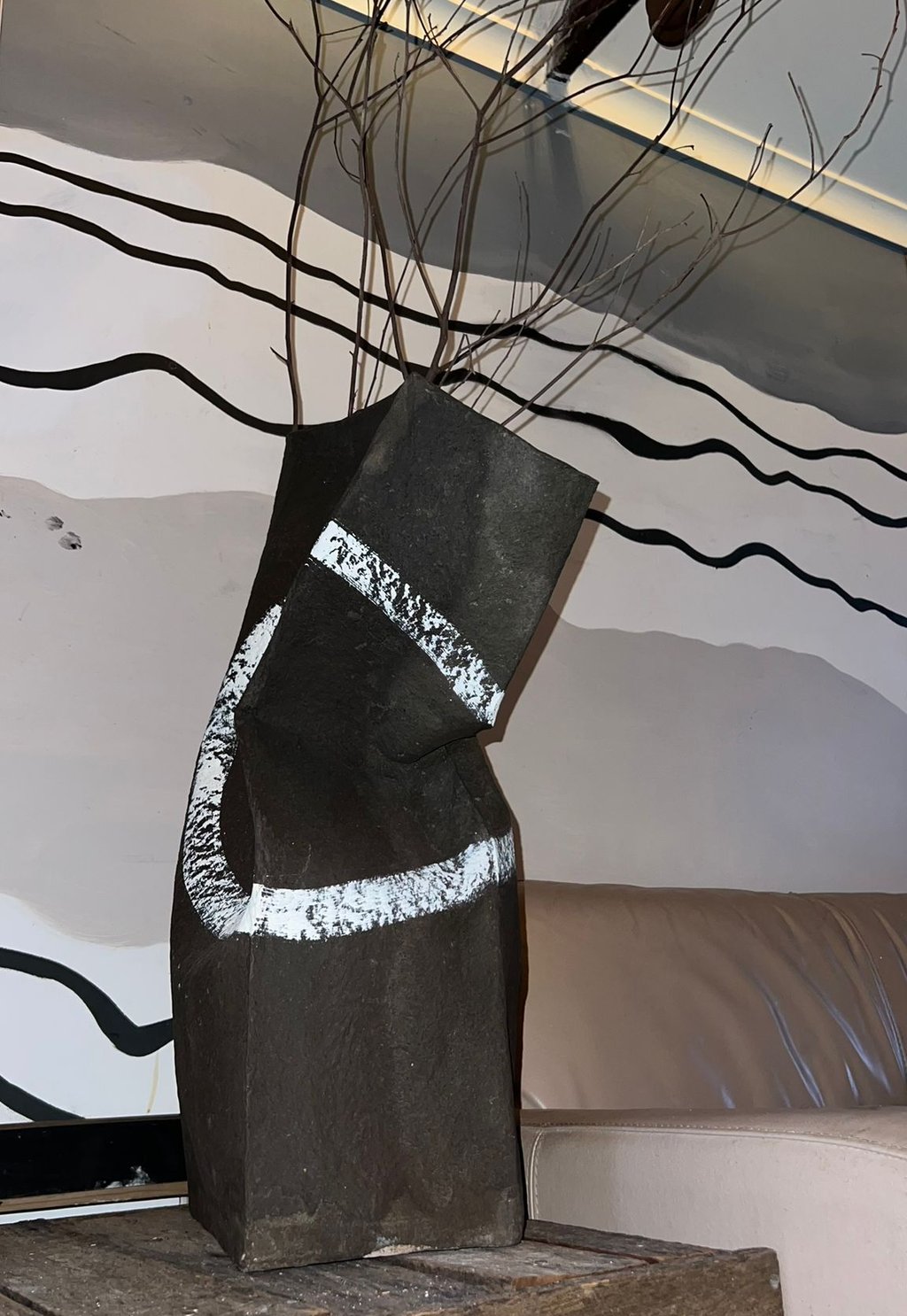A modern black ceramic vase with abstract white stripes holds dry branches on a rustic wood table.