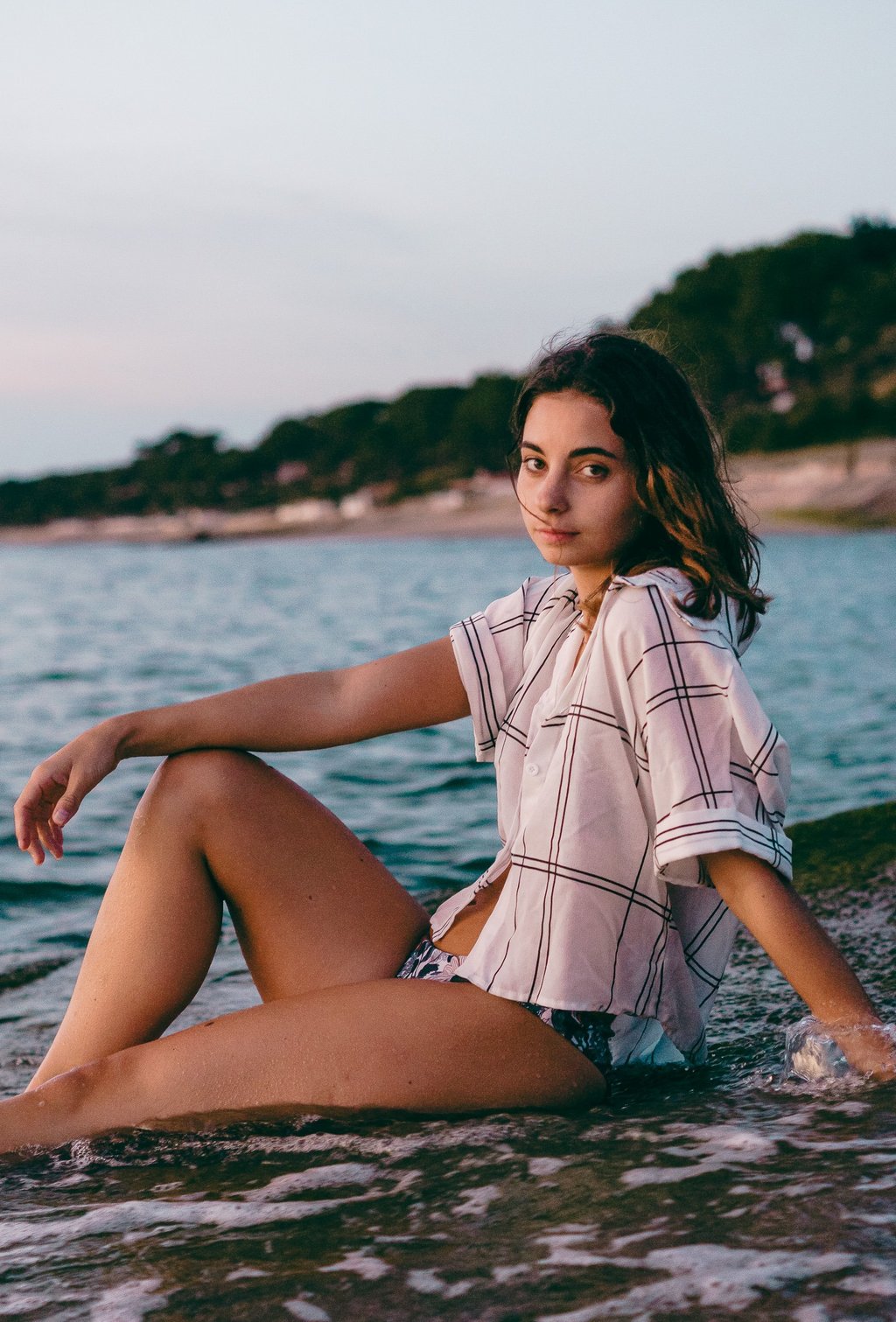 femme assise sur la plage portant une chemise et un maillot de bain regardant l'objectif 