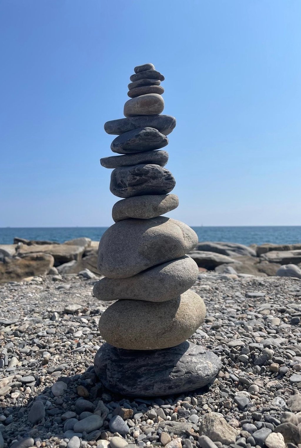 des galets empilés pour former un cairn avec en fond la mer et le ciel bleu