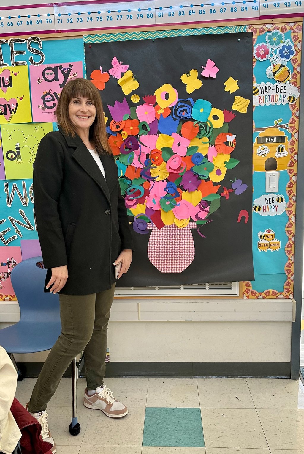 a teacher standing by a collage of paper flowers