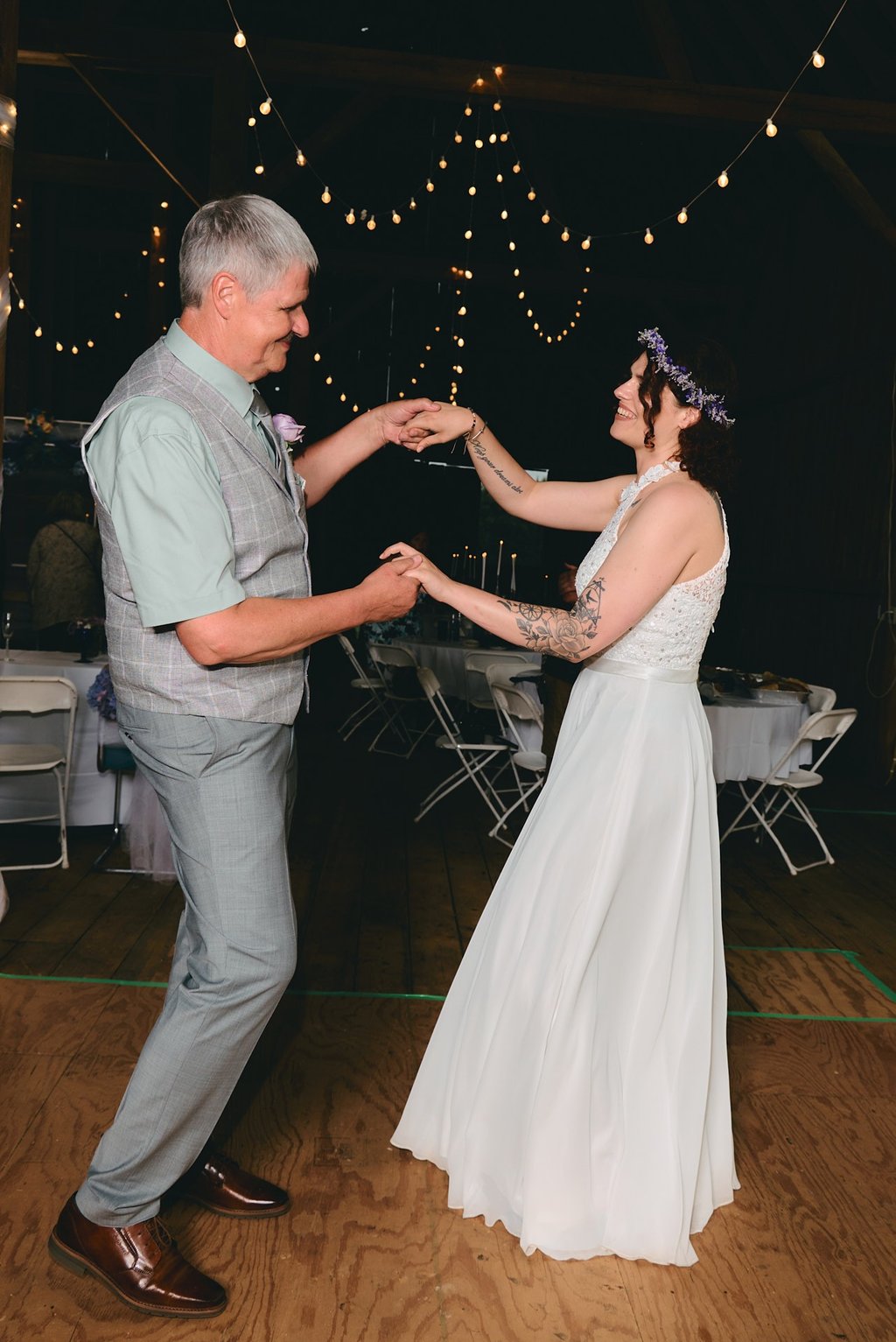 a bride and her father dancing at a wedding in a barn