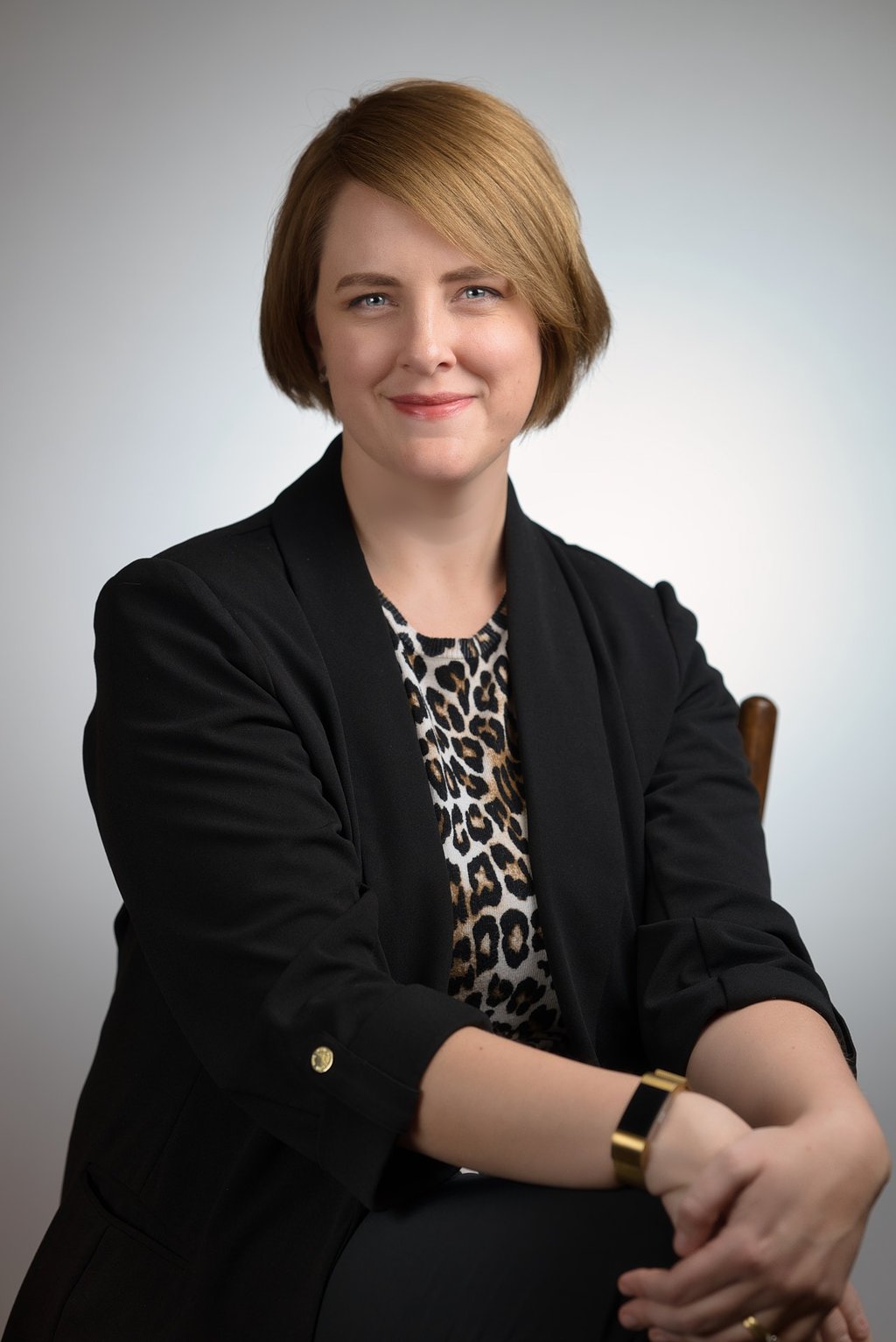 a woman in a black jacket and leopard print top sitting in front of a white background