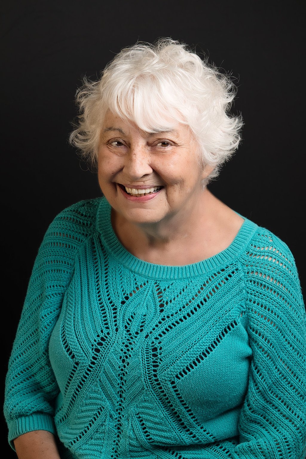 a woman with white hair and a blue sweater with big smile
