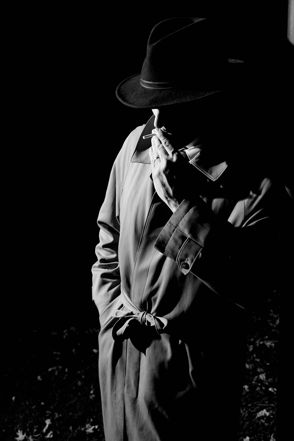 a man in a hat and coat jacket smoking in film noir style