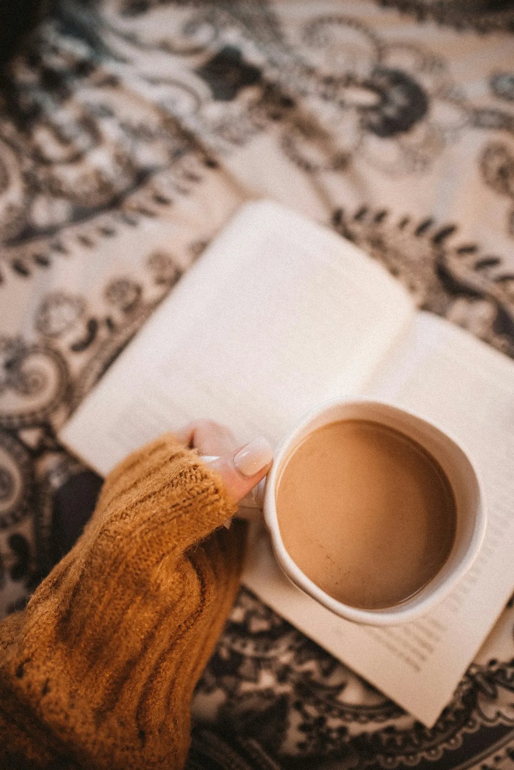 Main de femme tenant une tasse de café sur un livre, symbole d’ancrage doux et d’exploration intérie