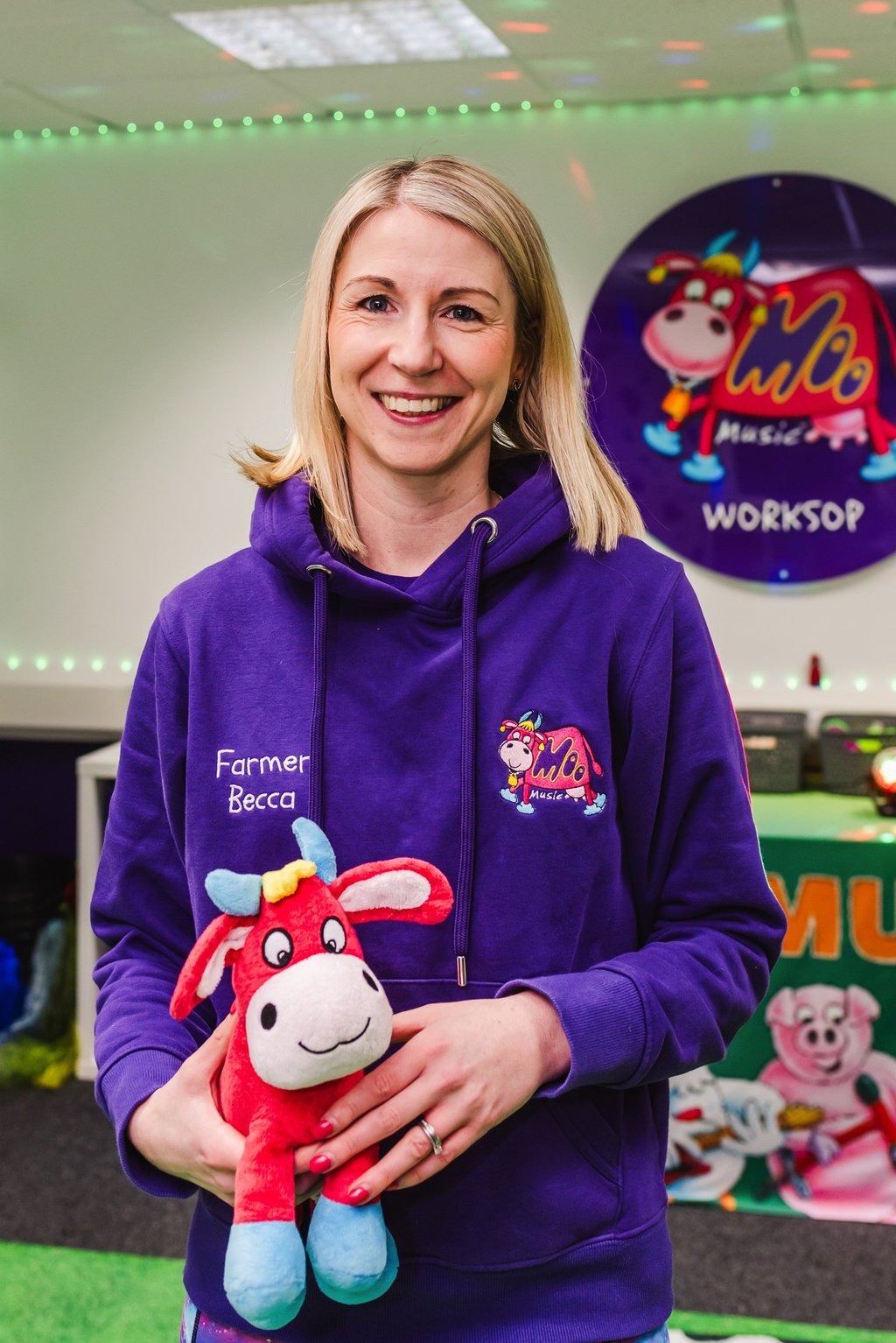 Farmer Becca stood in the Moo Room smiling, holding Maggie Moo in her branded purple Moo hoodie.