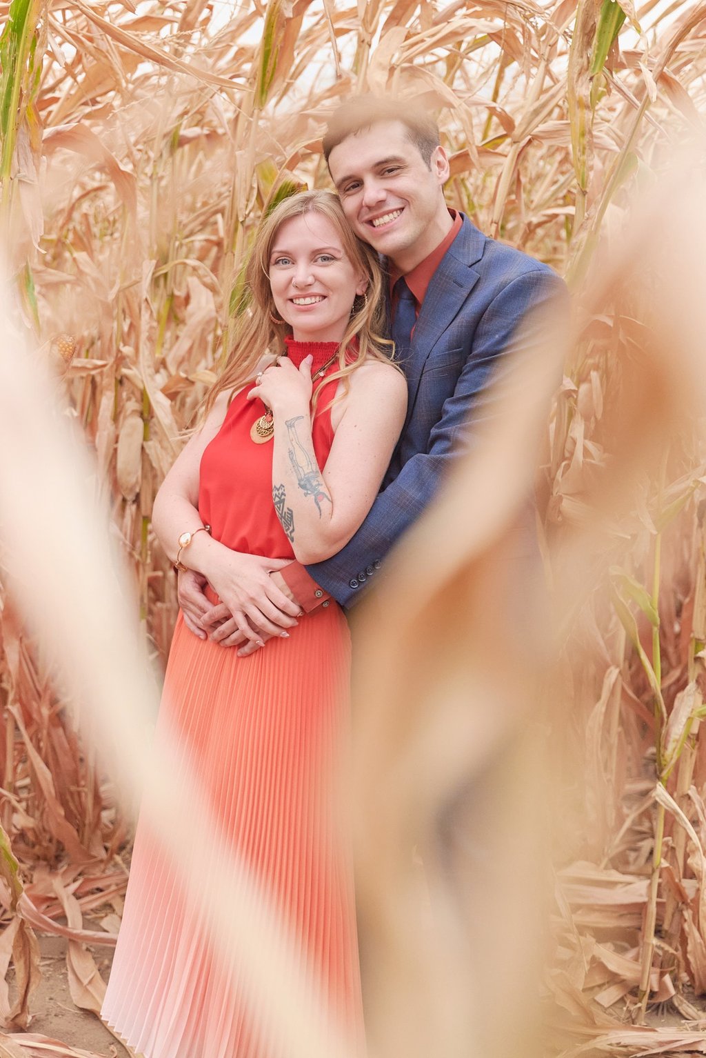 a man and woman standing in front of a corn field and hugging each other