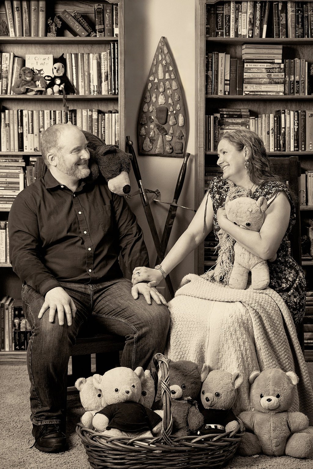 a man and a woman sitting on a chair holding a teddy bear in a library room