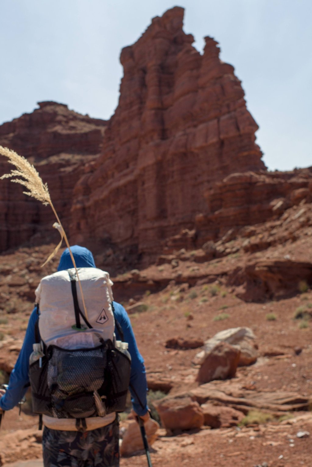 A hiker with a Hyperlite backpack walks toward a massive red rock formation in a desert canyon.