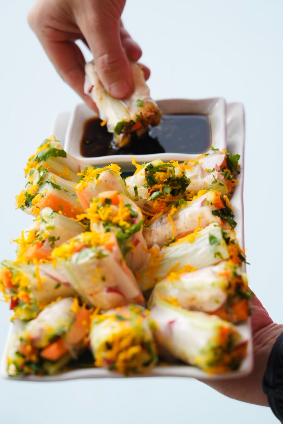 a person holding a plate with food and dipping sauce