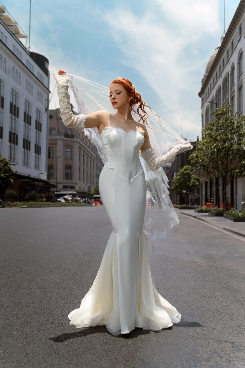 Redheaded bride in a mermaid wedding dress and lace veil posing on a city street.