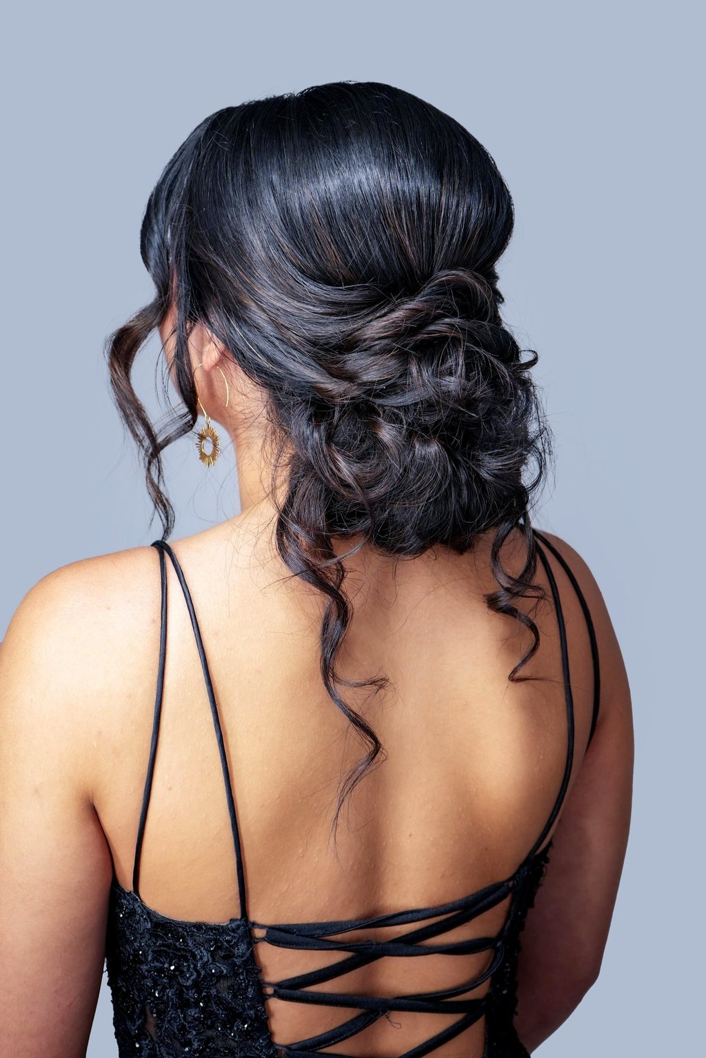 Woman with textured low bun updo and loose curls wearing black strappy dress, elegant hairstyle perfect for wedding or prom.