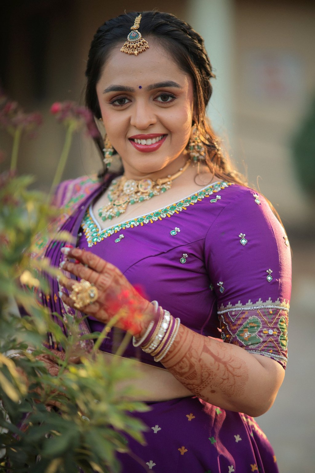 "Smiling Indian bride with traditional bridal makeup, maang tikka, and purple lehenga saree in outdo