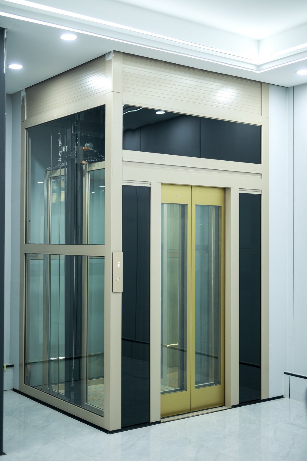 Modern residential glass elevator with gold trim and a beige metal frame installed in a luxury home.