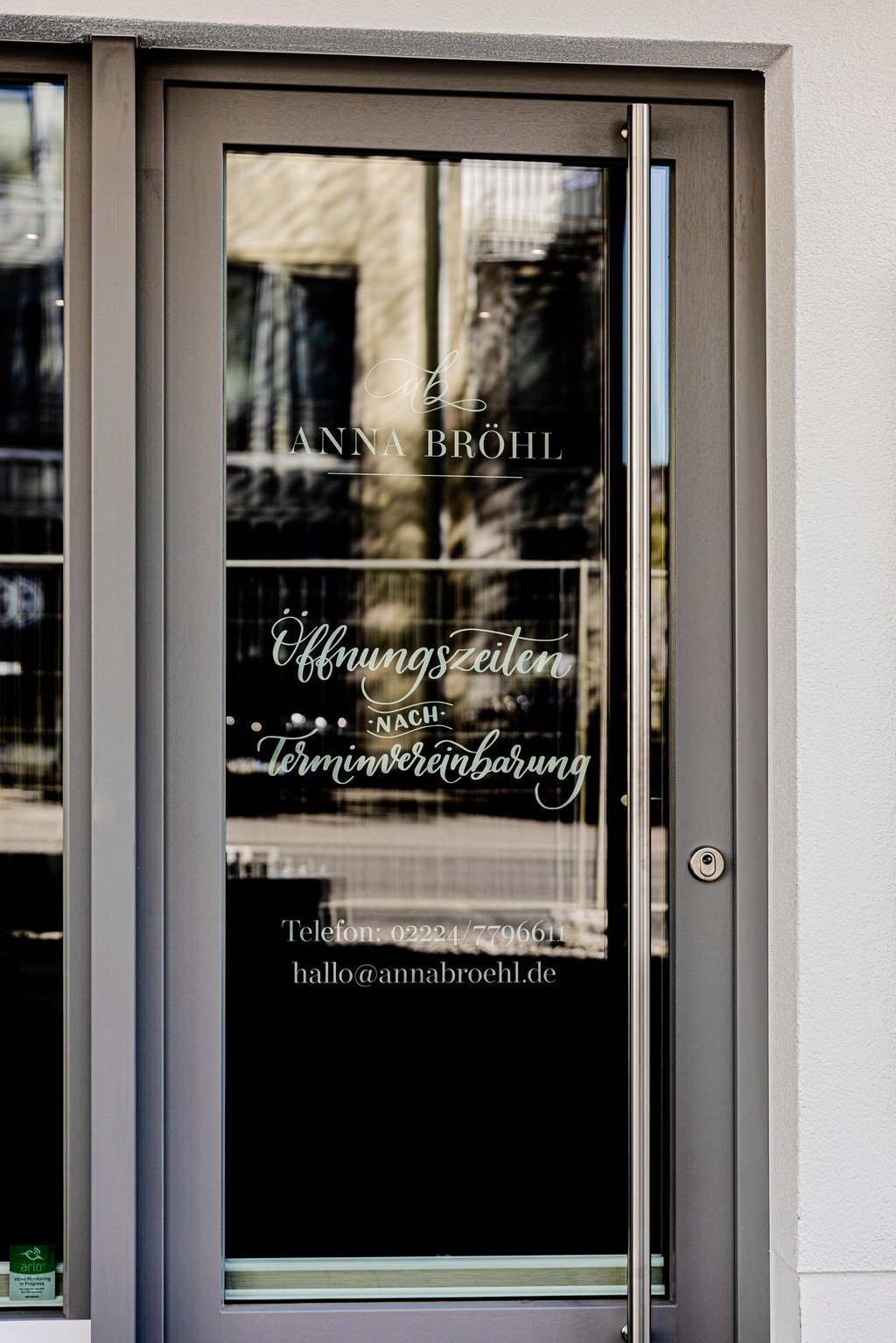 Glass entrance door to Anna Bröhl studio showing opening hours by appointment and contact details.