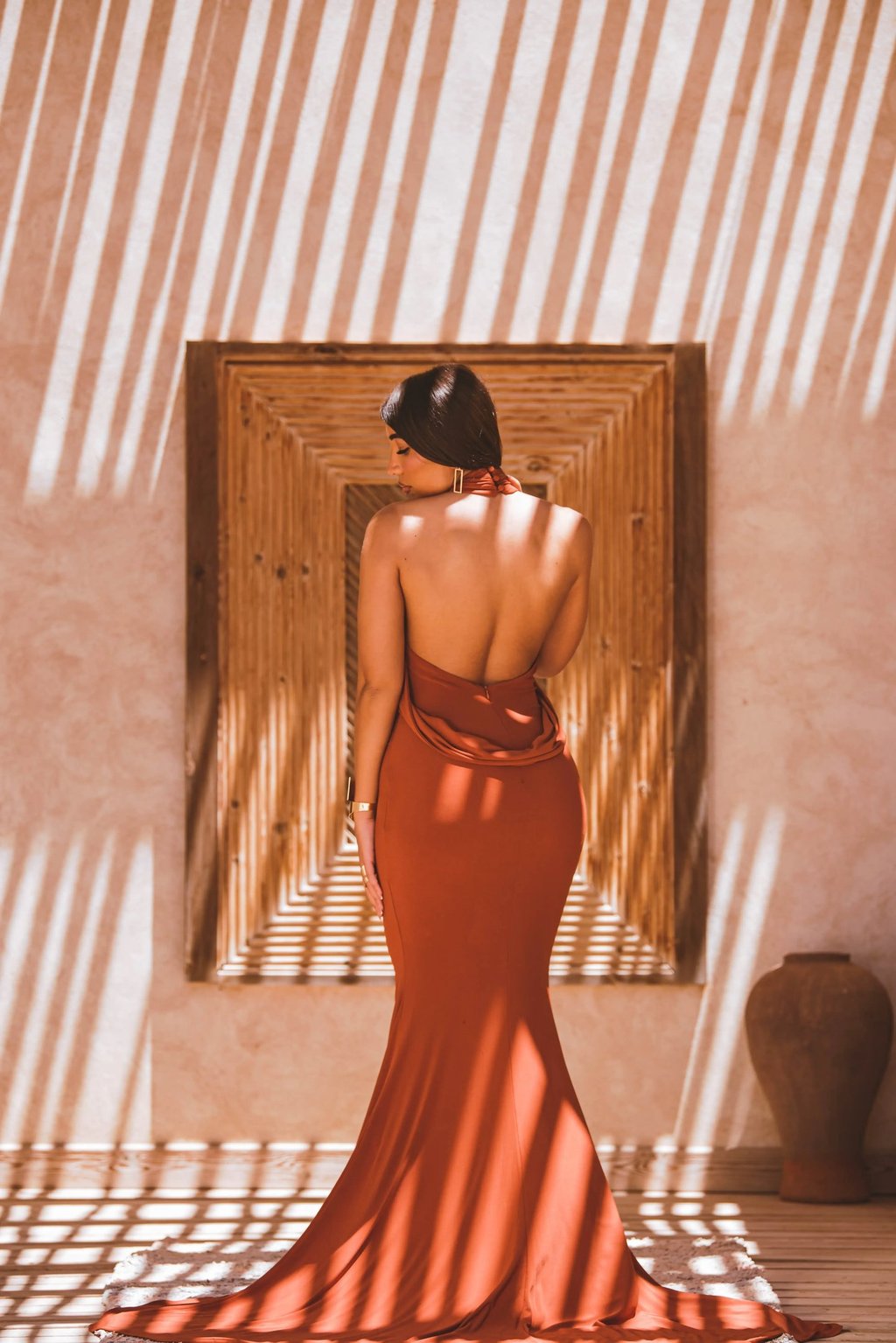 High-fashion portrait in Dakhla showing geometric shadow play on a resort wall with a model in an elegant backless dress.