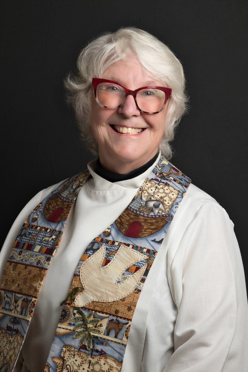 a woman in a clergy outfit and red glasses smiling