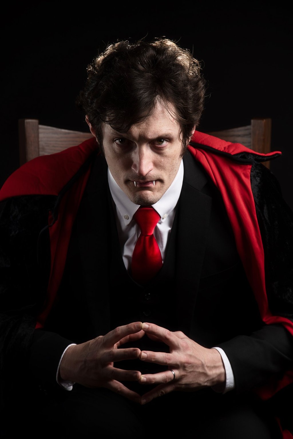 a man in a vampire suit with vampire teeth out and tie with a red tie  