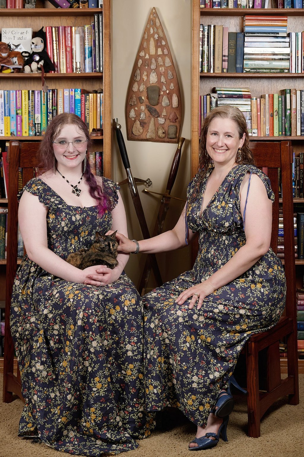 a mother and a daughter in matching dresses with a cat are posing for a photo