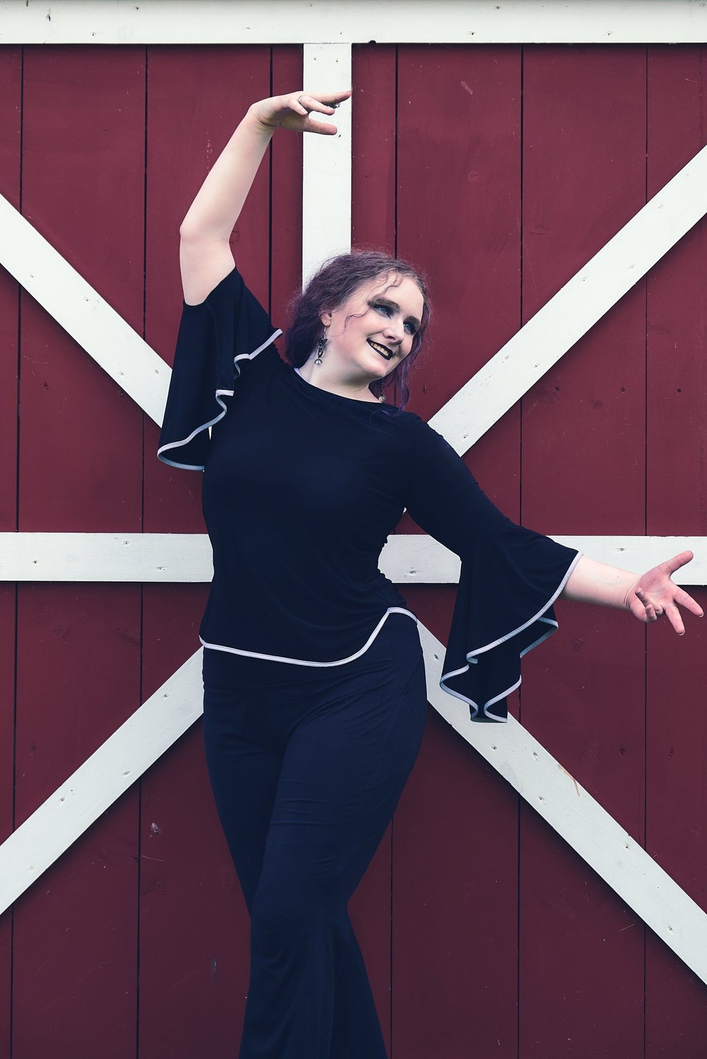 a woman in a black top and pants dancing in front of a barn