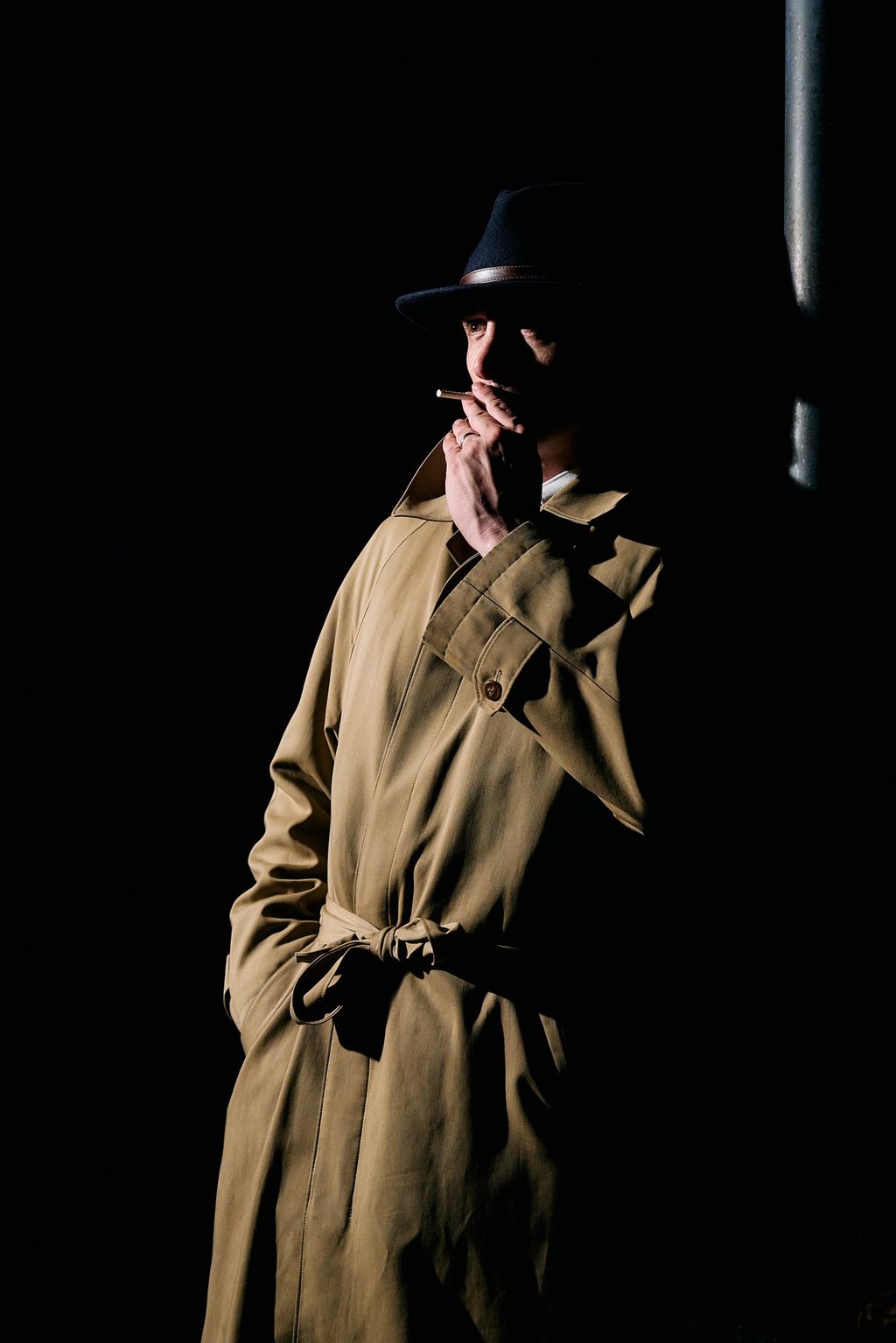 a man in a trench coat with a blue hat smoking a cigarette