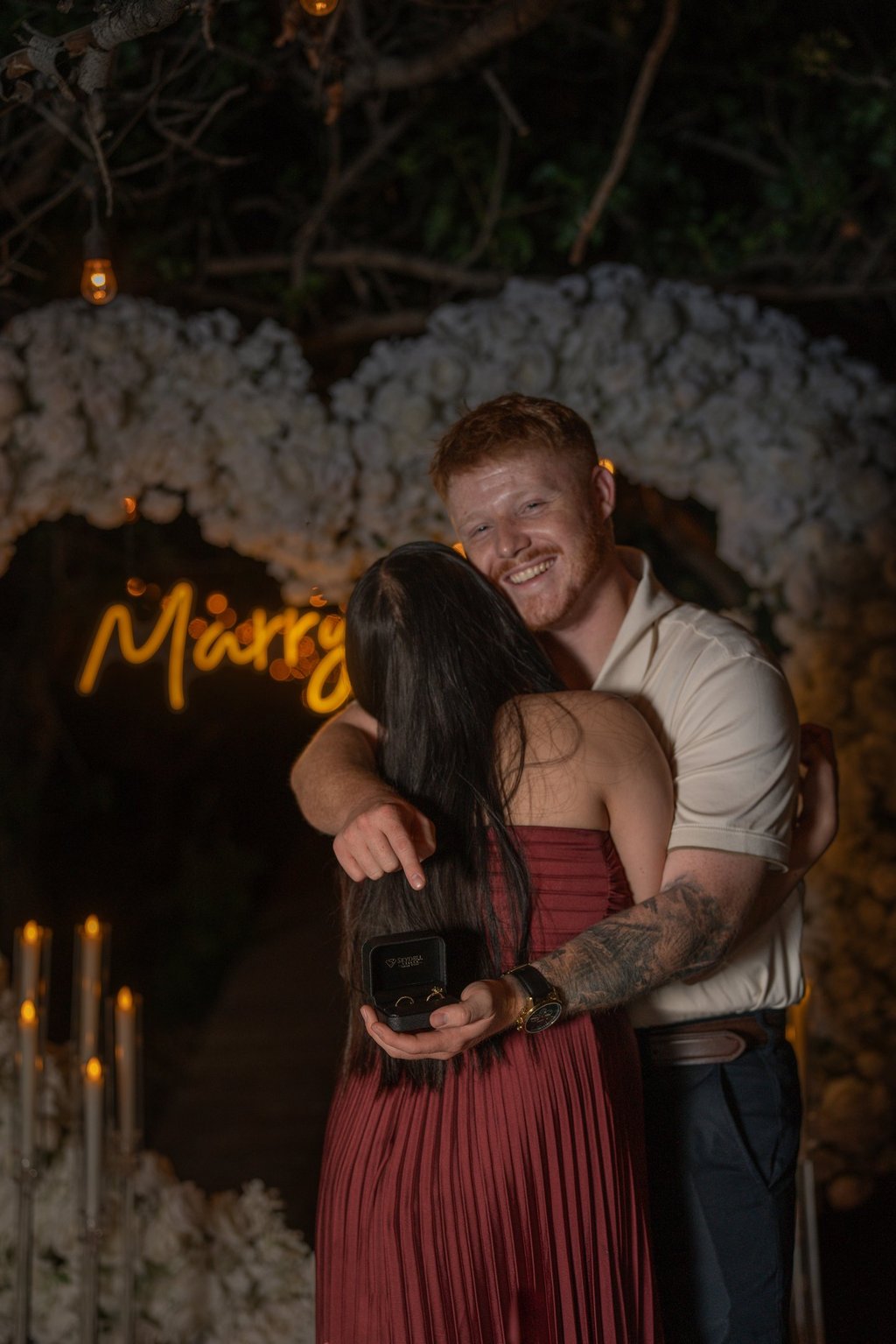 a man and woman embracing in front of a neon sign