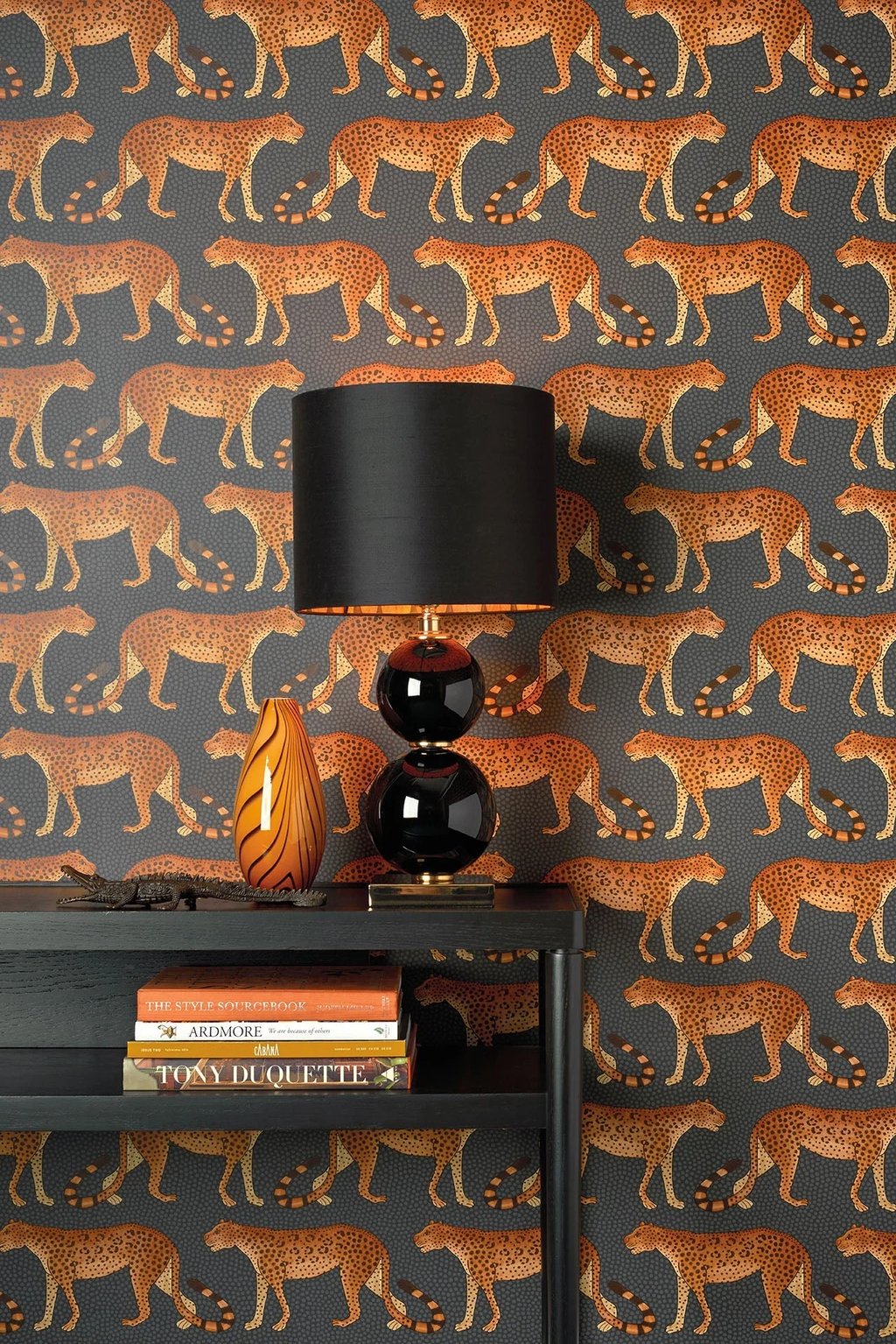 Modern interior featuring leopard print wallpaper with a black table lamp and stacked coffee table books.