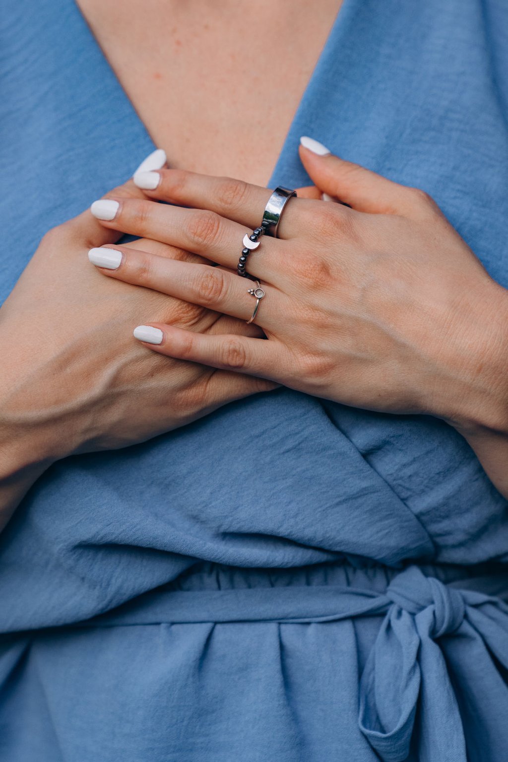 Woman with wearing silver moon and star rings over a blue wrap dress.
