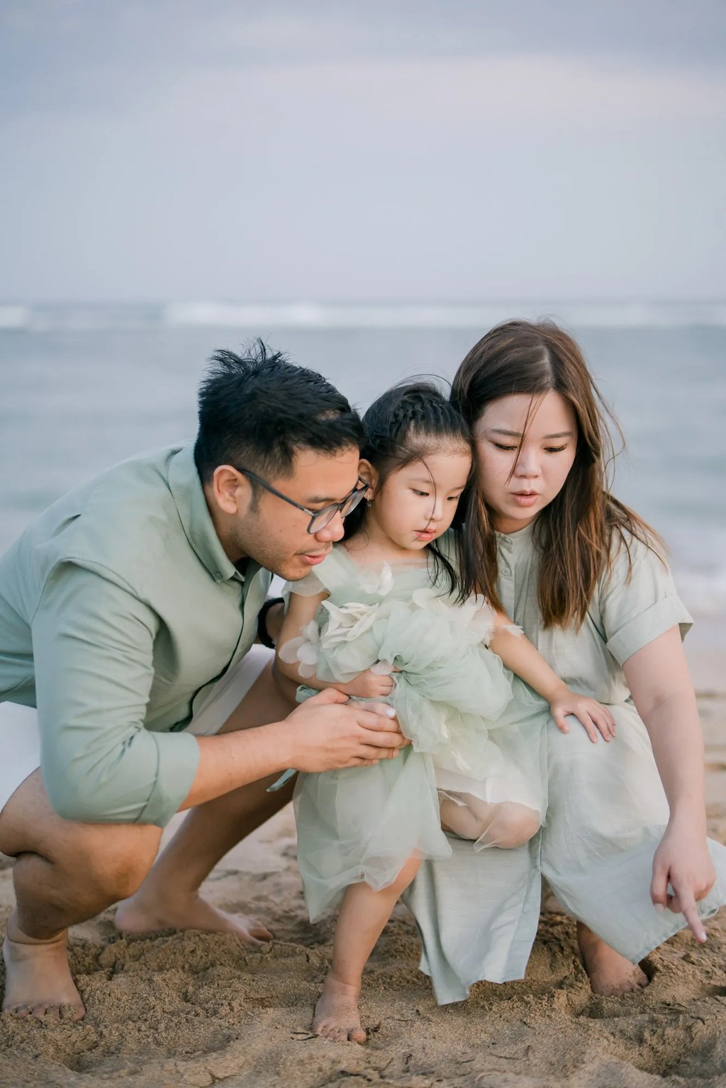 Parents sharing a tender moment with their daughter during a beach family photography session in Bali.