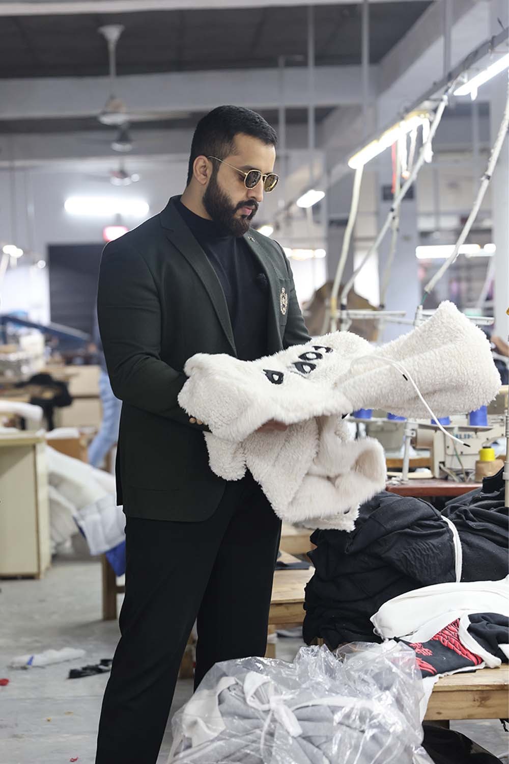 a man in a suit jacket is holding a sherpa fleece hoodie in a manufacturing  factory