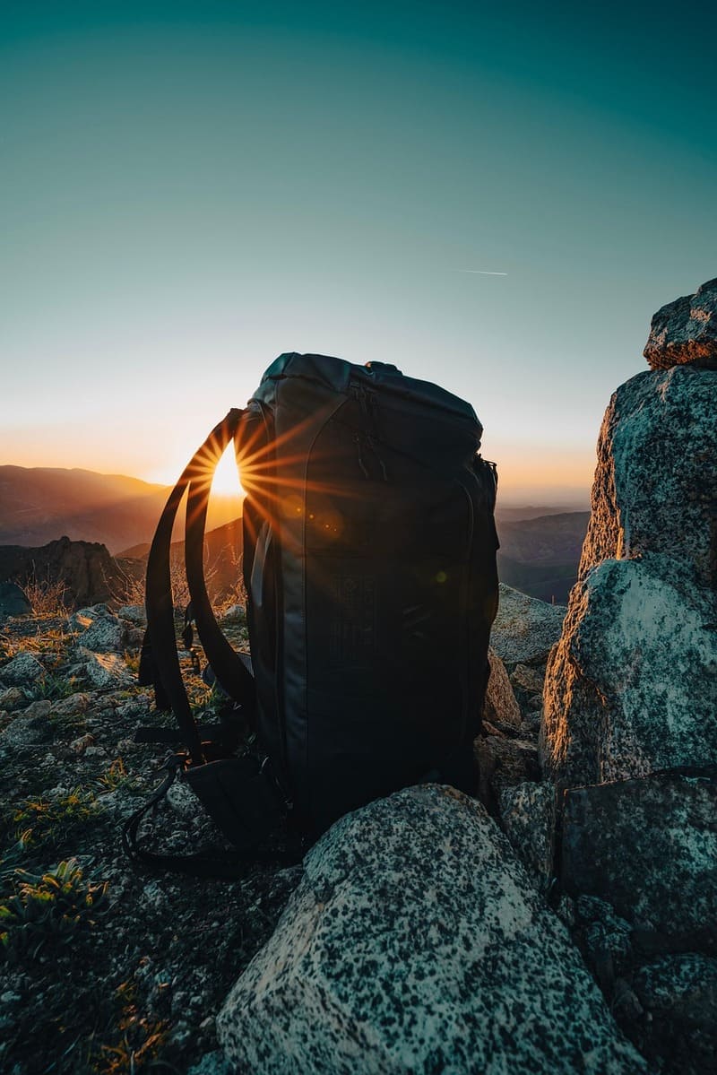 Schwarzer Outdoor-Rucksack auf einem felsigen Berggipfel bei Sonnenuntergang – Wanderabenteuer