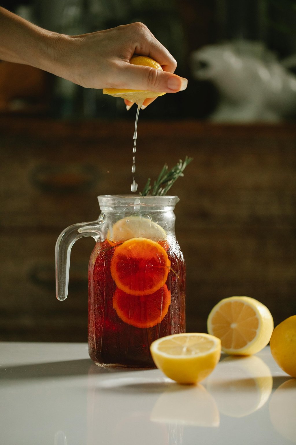 a person squeezing lemonade into a jar of cold tea