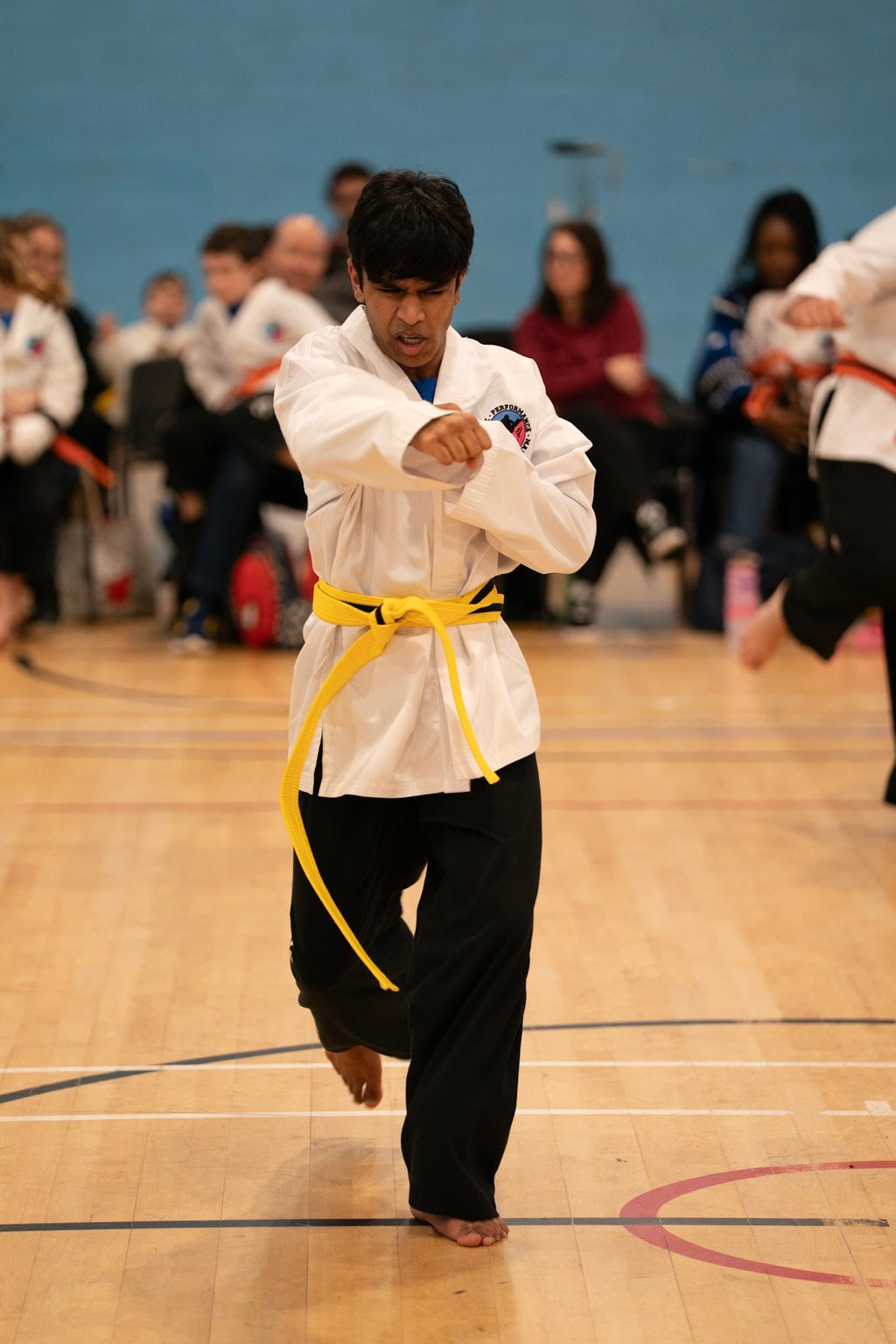 A young martial artist in a white uniform and yellow belt performs a karate punch at a competition.
