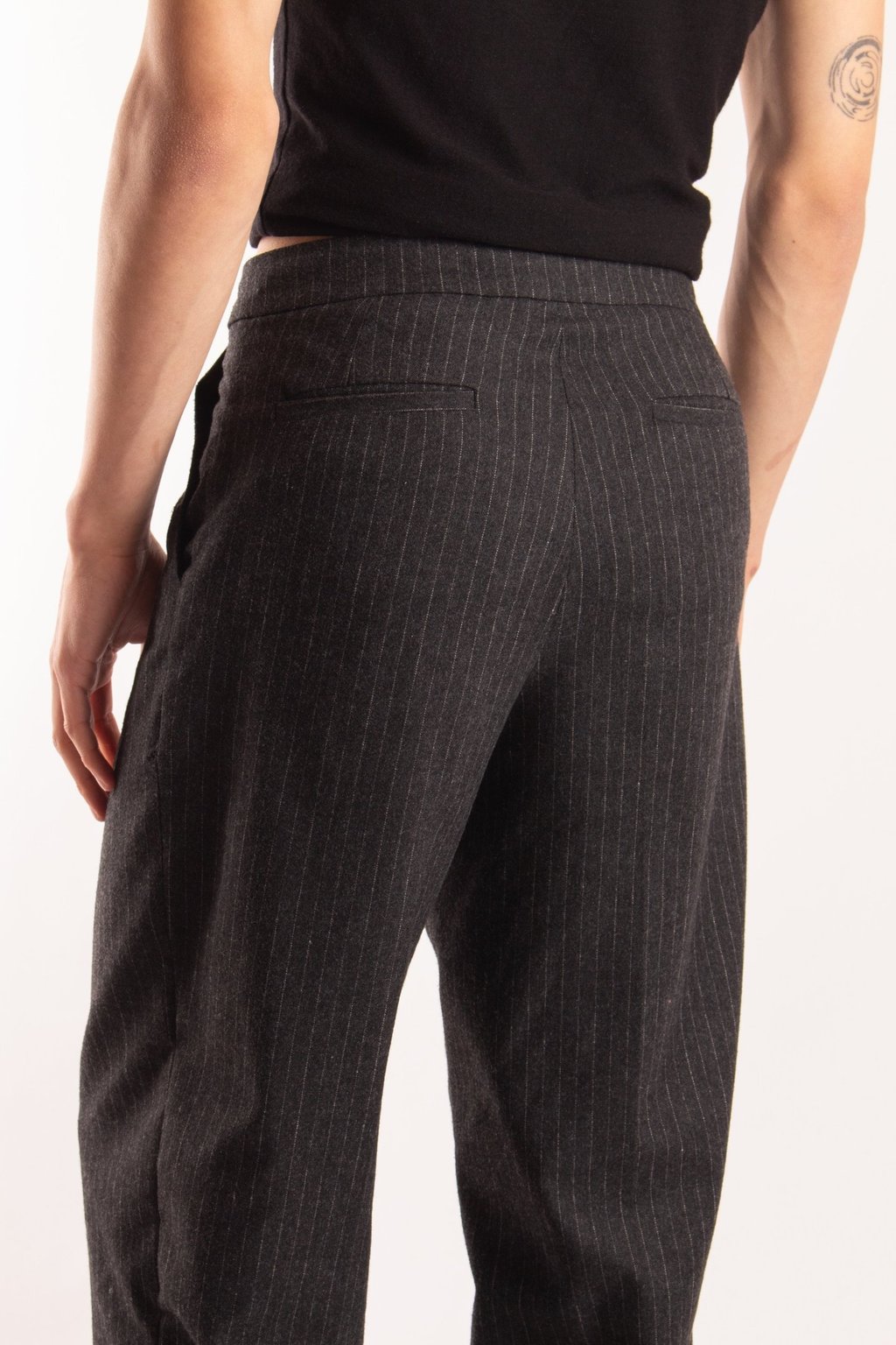 Back view of a person wearing dark grey pinstripe dress pants and a black t-shirt.