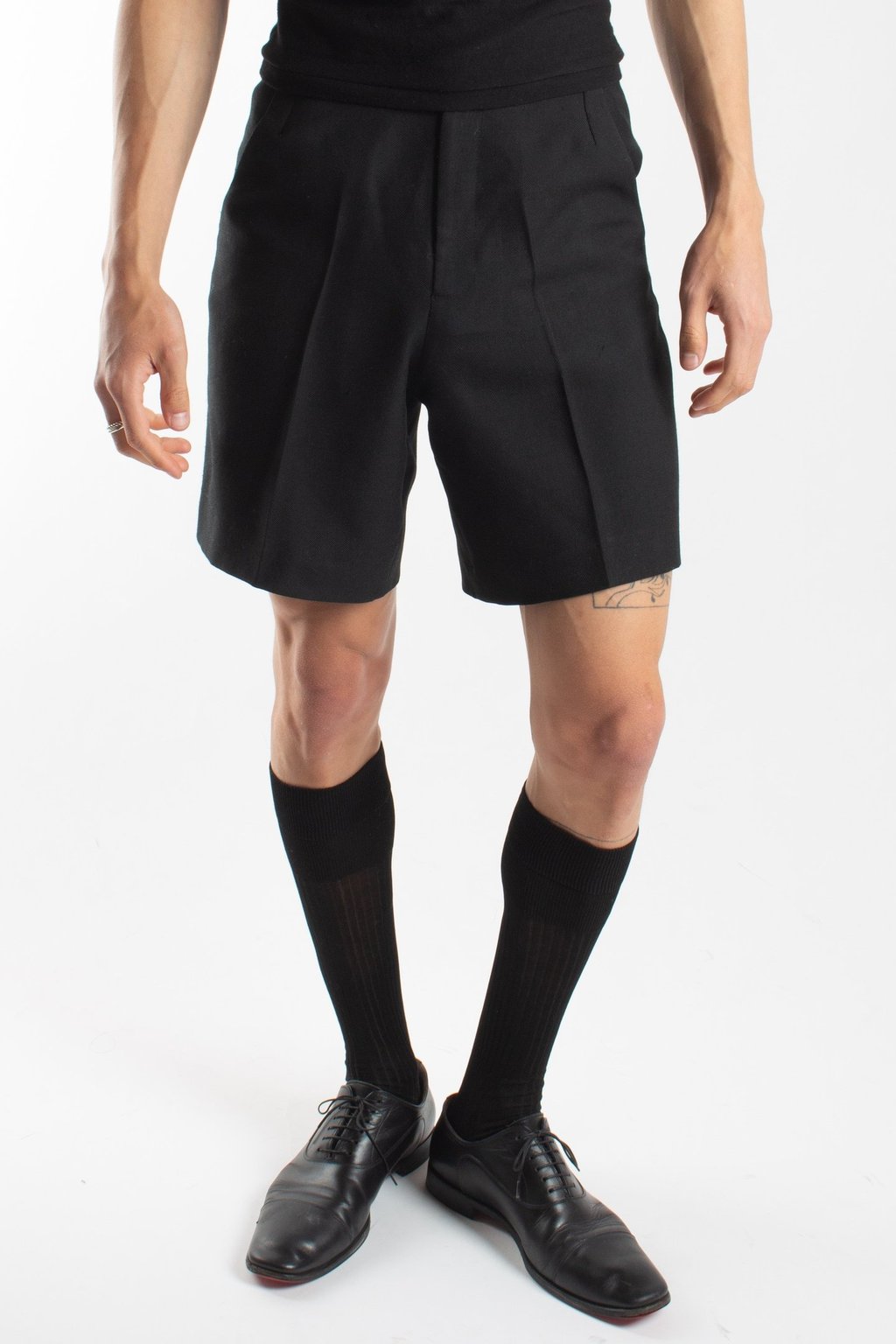 Model wearing black tailored dress shorts, knee-high socks, and leather oxford shoes.