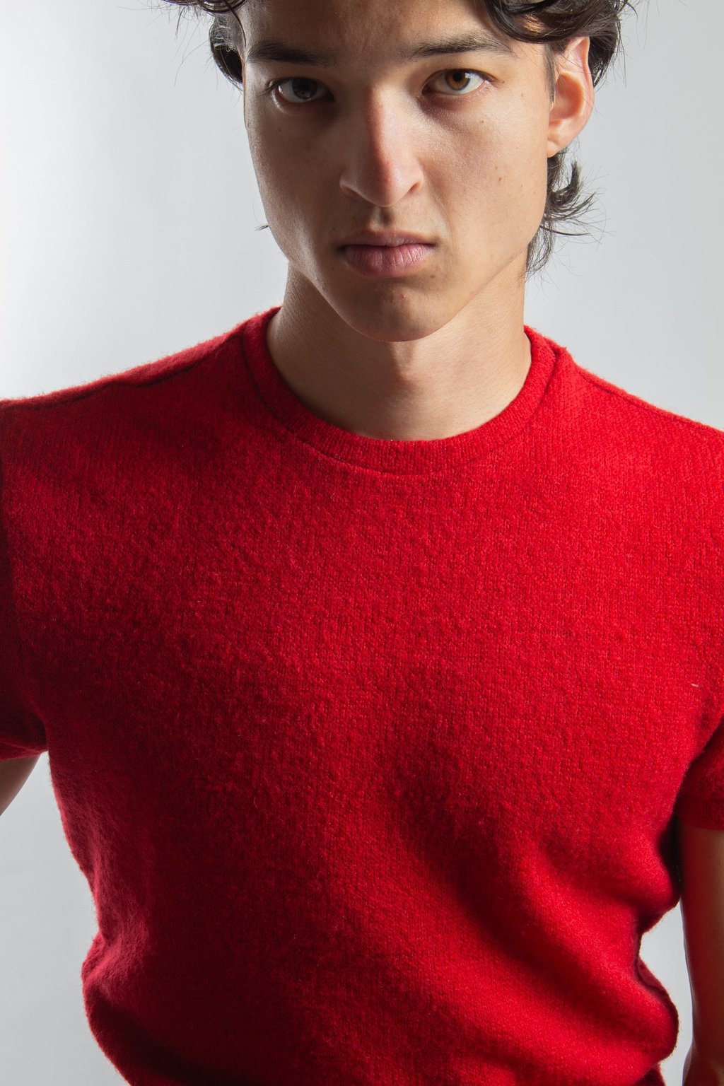 Young man wearing a bright red wool knit crewneck sweater against a plain grey background.