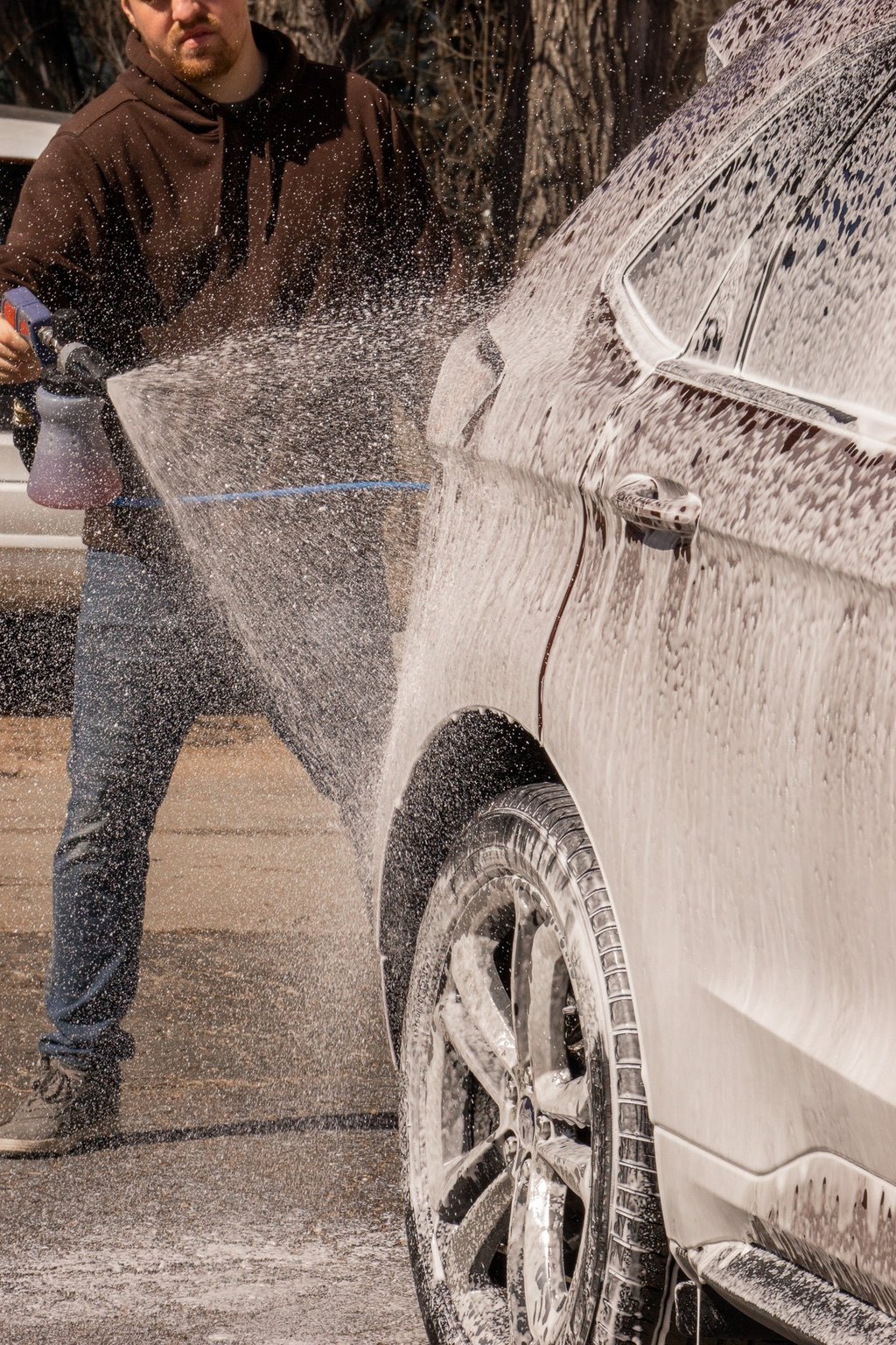 A man uses a high-pressure foam cannon to apply thick car wash soap to a vehicle.