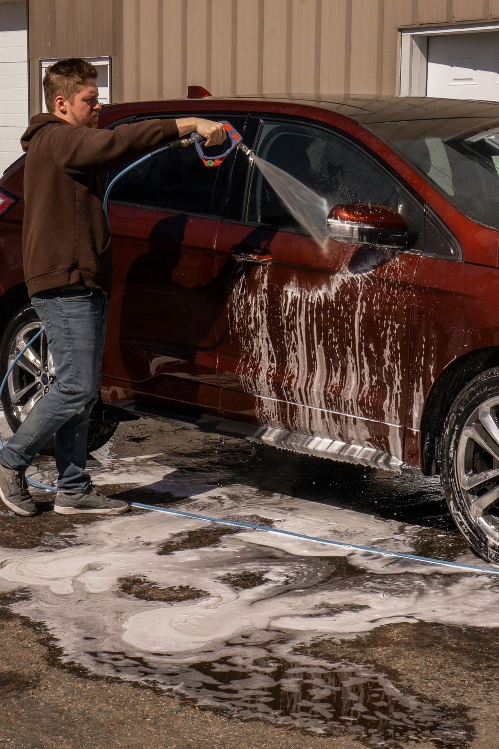 A man uses a pressure washer to rinse soap off a red SUV during a professional car wash service.
