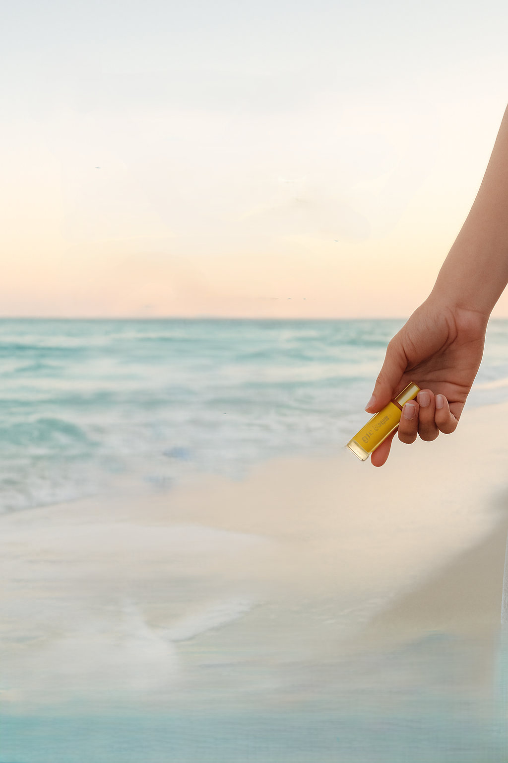 image of hand holding an essential oil bottle beachside