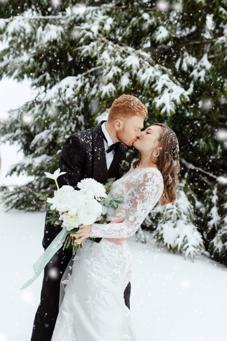 a bride and groom kissing in the snow