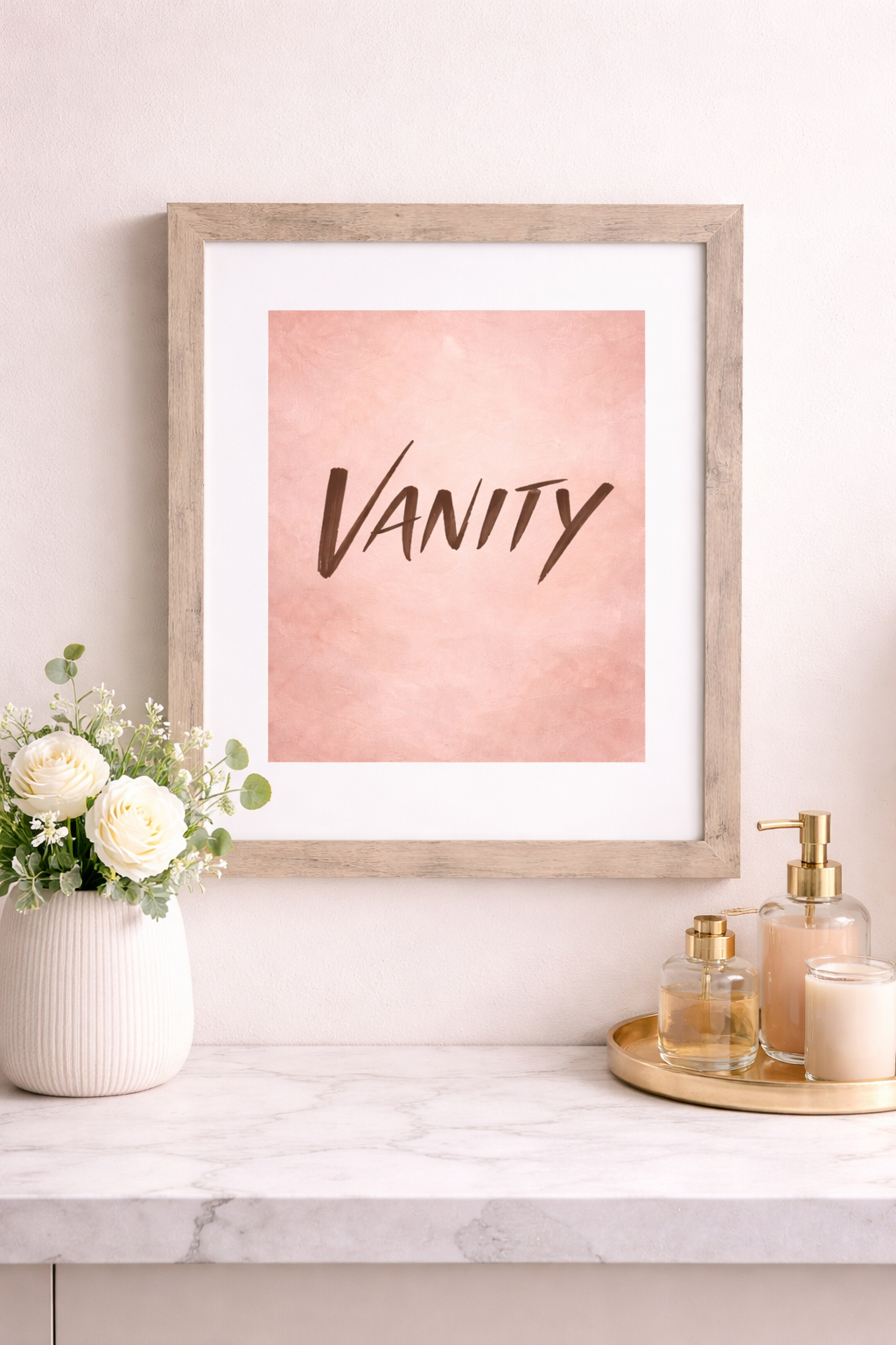 Framed pink Vanity wall art print on a marble table with white roses and gold perfume bottles.