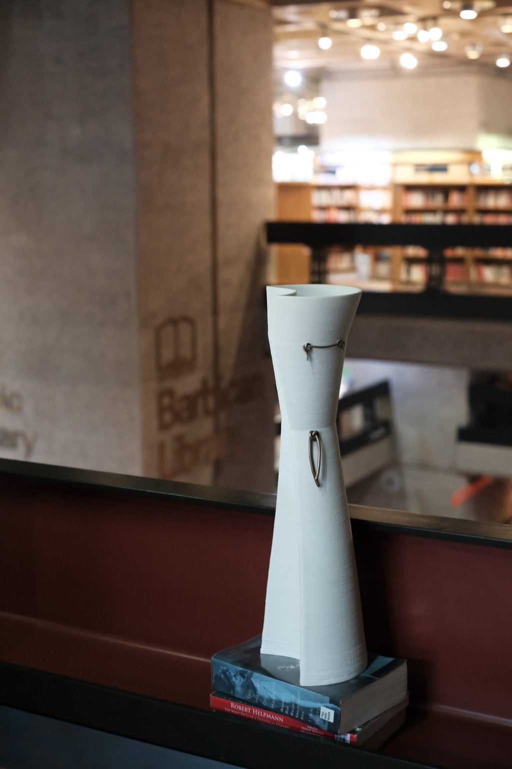A tall elegant white porcelain vessel, with bronze knot details, on a shelf in the Barbican Library