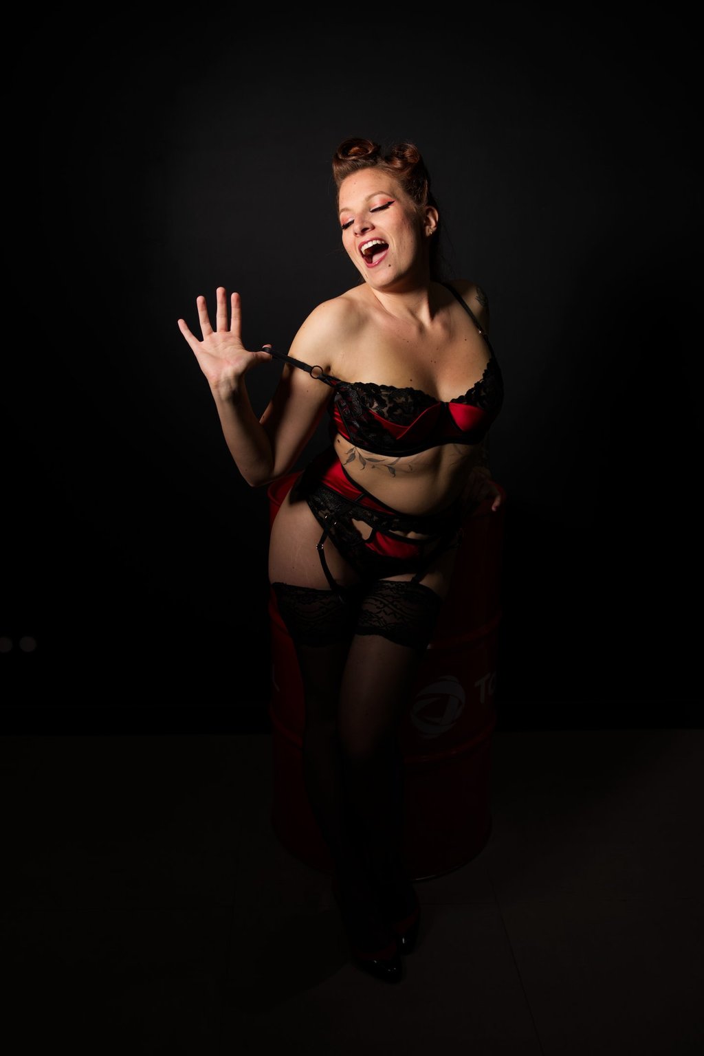 Glamour. Femme en lingerie rouge et noire qui se déshabille en souriant.
