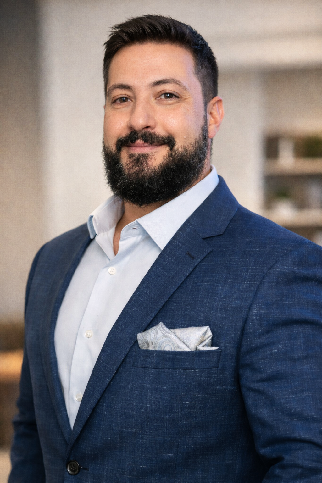 Professional man with a beard wearing a blue suit jacket and pocket square for a corporate headshot.