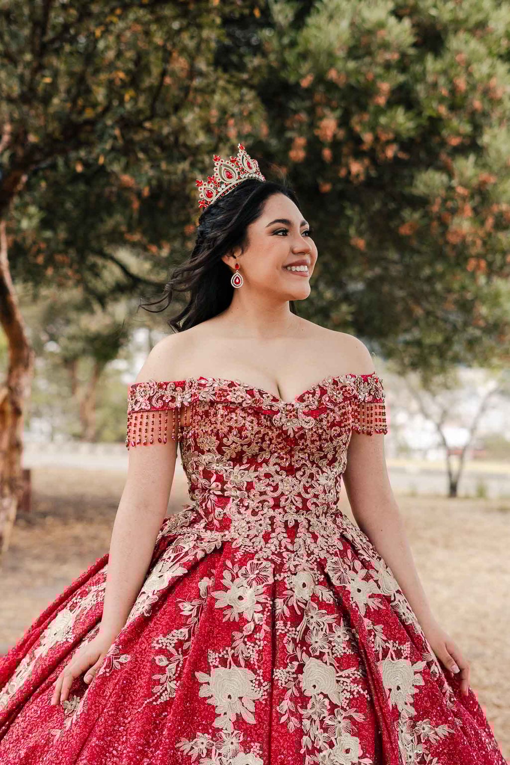 Hermoso retrato profesional de quinceaños con vestido rojo en Itchimbía Quito con naturaleza y sonrisa de felicidad