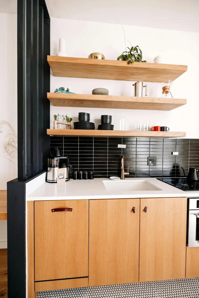 Modern kitchen with natural wood cabinets, floating shelves, and black subway tile backsplash.