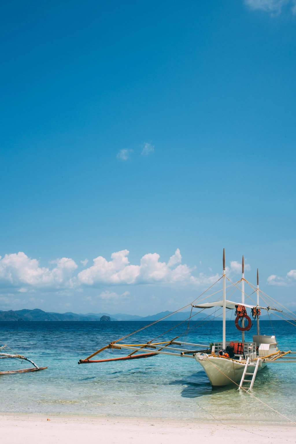 Traditional Filipino outrigger boat on a sereme tropical beach with clear blue water and distant islands under a bright sky