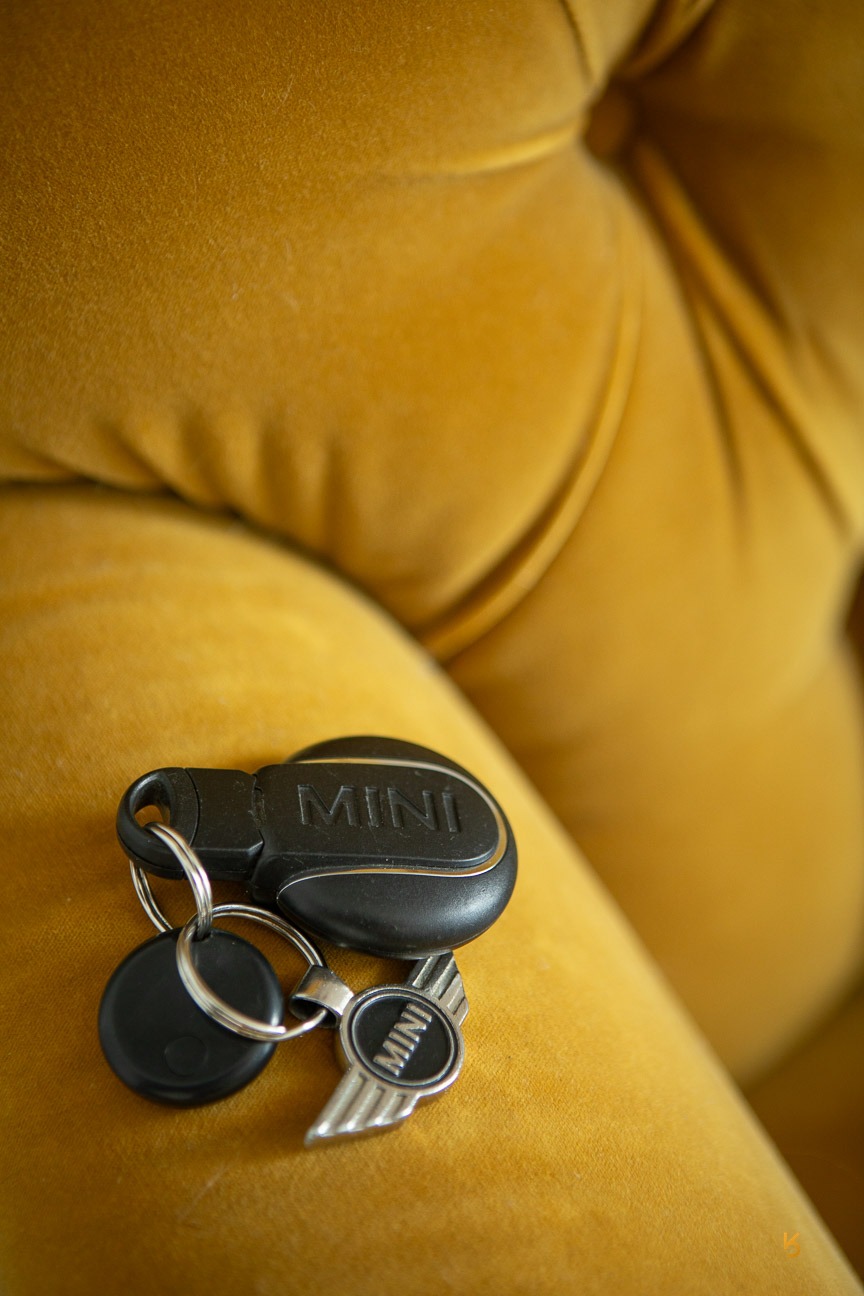 Black Mini Cooper car key fob and silver logo keychain resting on a yellow velvet couch.