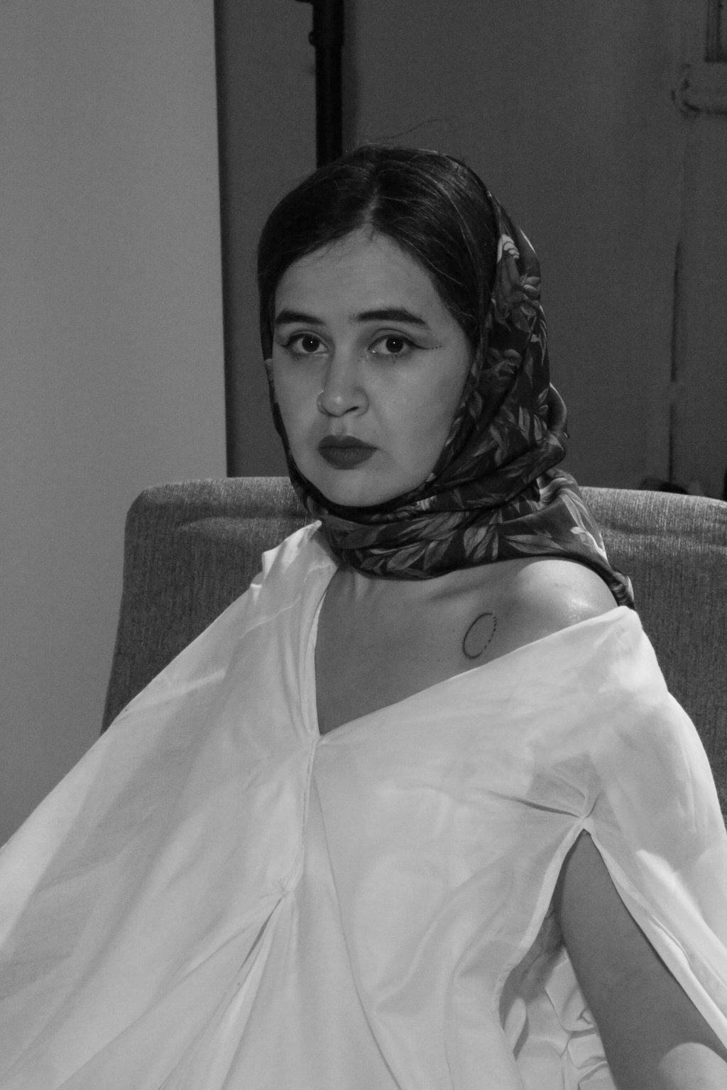 Black and white portrait of a woman wearing a floral headscarf and off-the-shoulder white blouse.