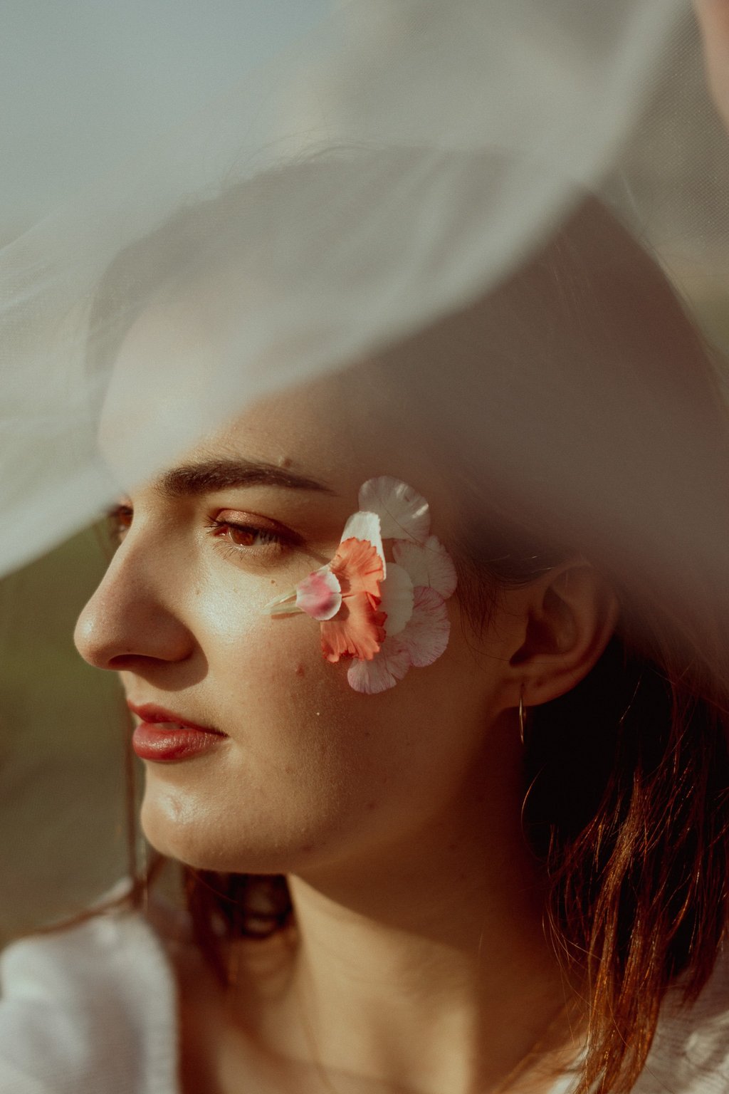 portrait rapproché d'un visage féminin de profil maquillé recouvert d'un voile en tulle transparent